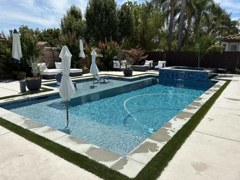 A clear backyard pool and spa surrounded by greenery, from the Oasis Pool Services collection